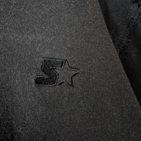 starter-brust-logo-stickerei-detail Nahaufnahme des gestickten Starter-Logos auf der Brust des schwarzen Hoodies.