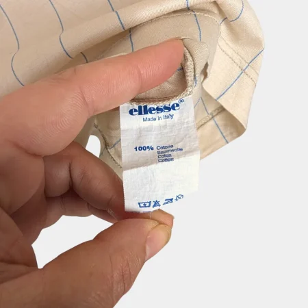 true-vintage-ellesse-polo-made-in-italy Vintage Ellesse Polo Hemd Detail des roten Webetiketts mit goldener Schrift und Made in Italy Herkunft.